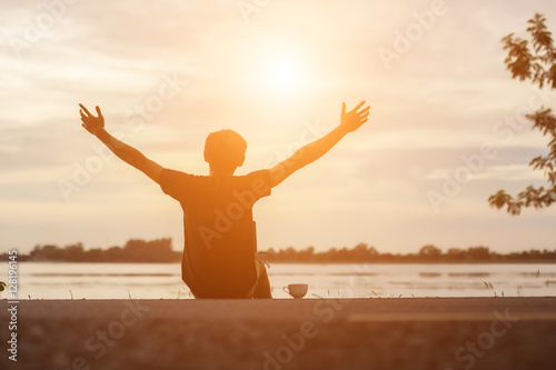 Successful sportsman raising arms on golden sky back lighting su