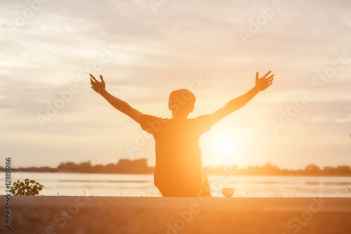 Successful sportsman raising arms on golden sky back lighting su