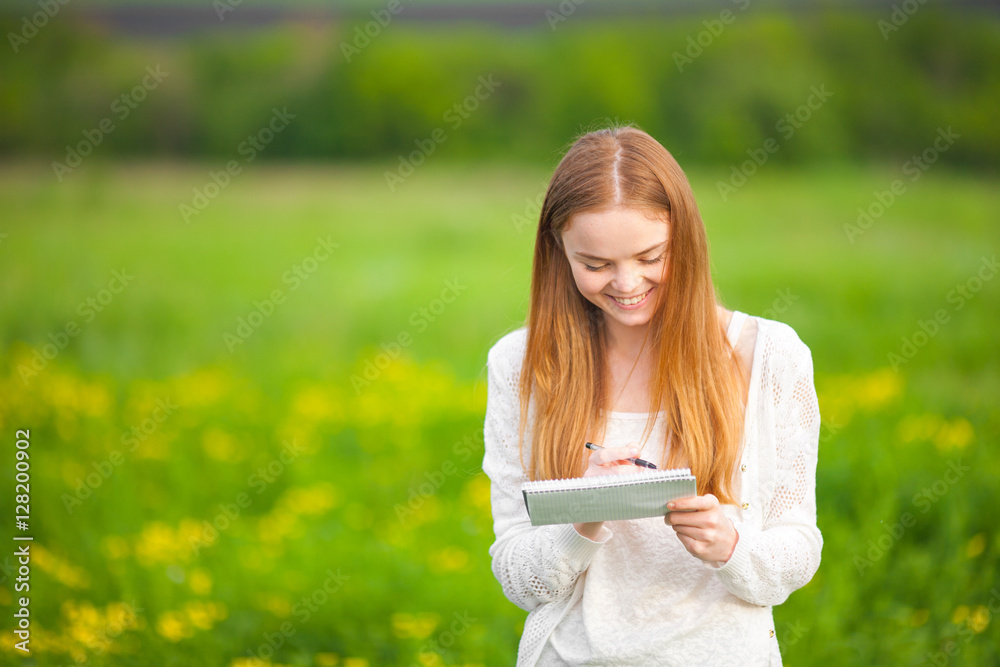 Young freckled girl agronomist or biologist in white blouse standing in green field with notebook and pen during harvest. Young freckled girl agronomist or biologist in white blouse standing in green field with notebook and pen during harvest.