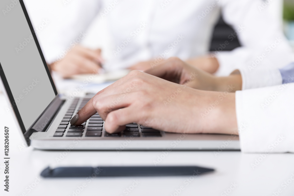 Woman is typing while her colleague in the background is writing Woman is typing while her colleague in the background is writing