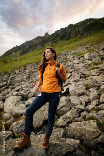 Young woman traveler with backpack relaxing outdoor with rocky mountains on background. Lifestyle hiking concept. Backpacker hiking at mountain peak