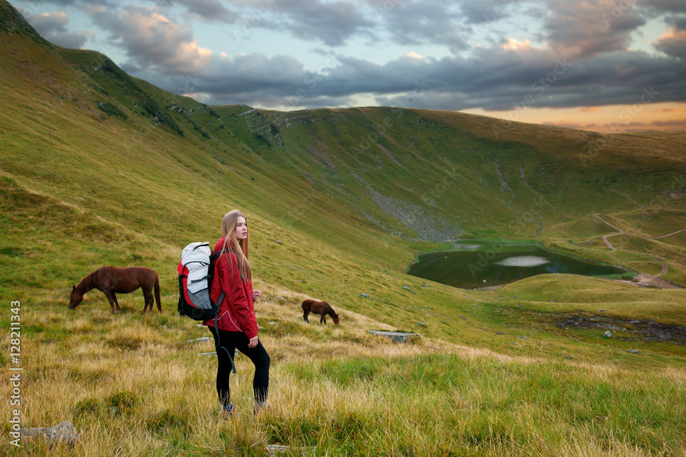 Portrait of a beautiful young woman looking at the landscape while hiking in a mountains with horses in the background