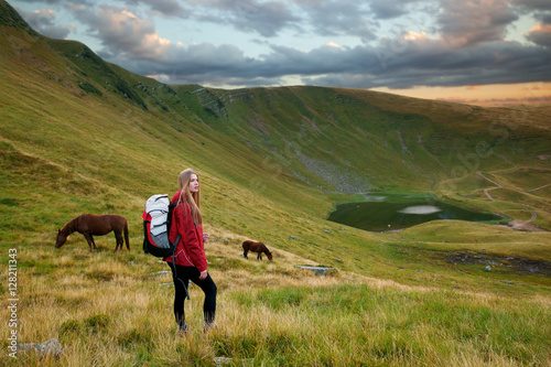Portrait of a beautiful young woman looking at the landscape while hiking in a mountains with horses in the background