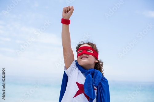 Boy in superhero costume with hand raised at beach