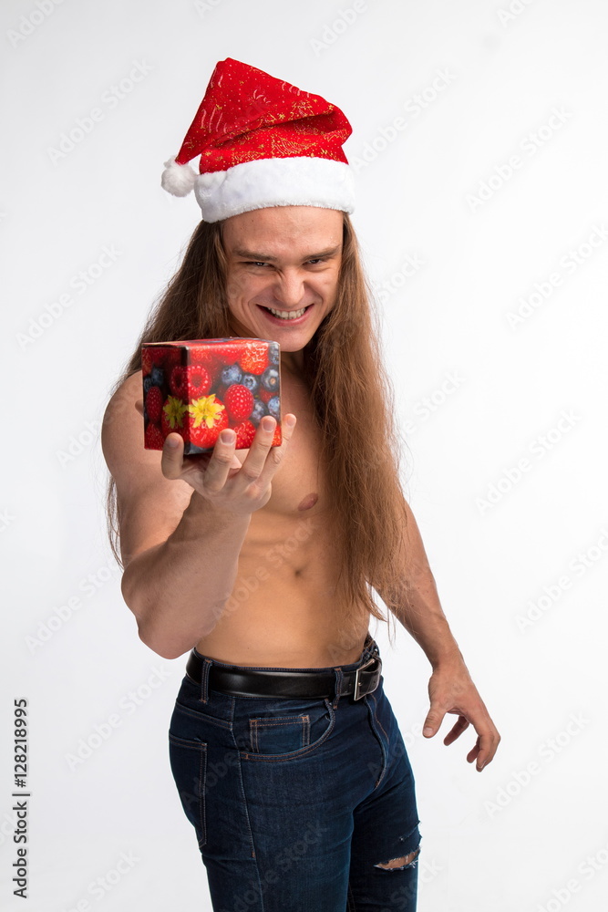 Athlete Bodybuilder Shirtless With Long Hair Posing In Cap Santa Claus With A Gift In Hand On