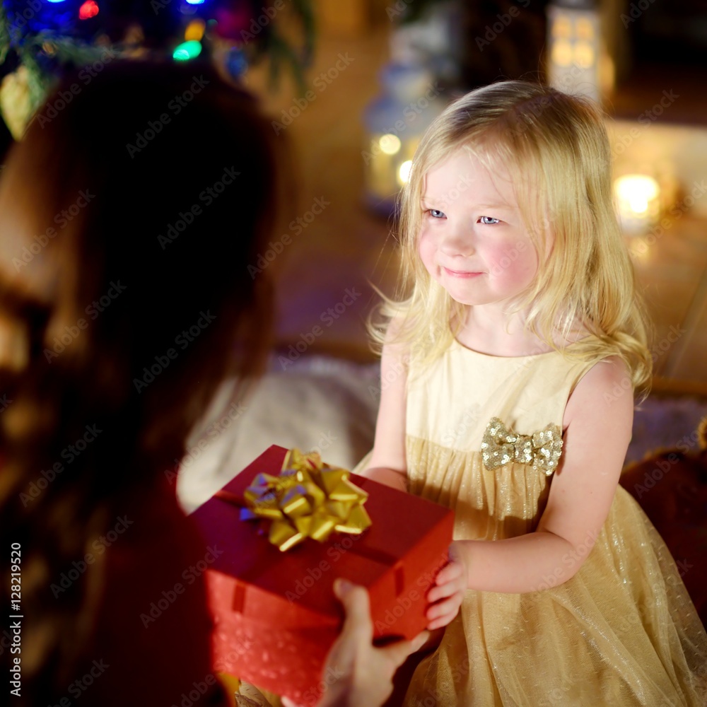 Happy little girl getting a Christmas gift from her mommy Happy little girl getting a Christmas gift from her mommy