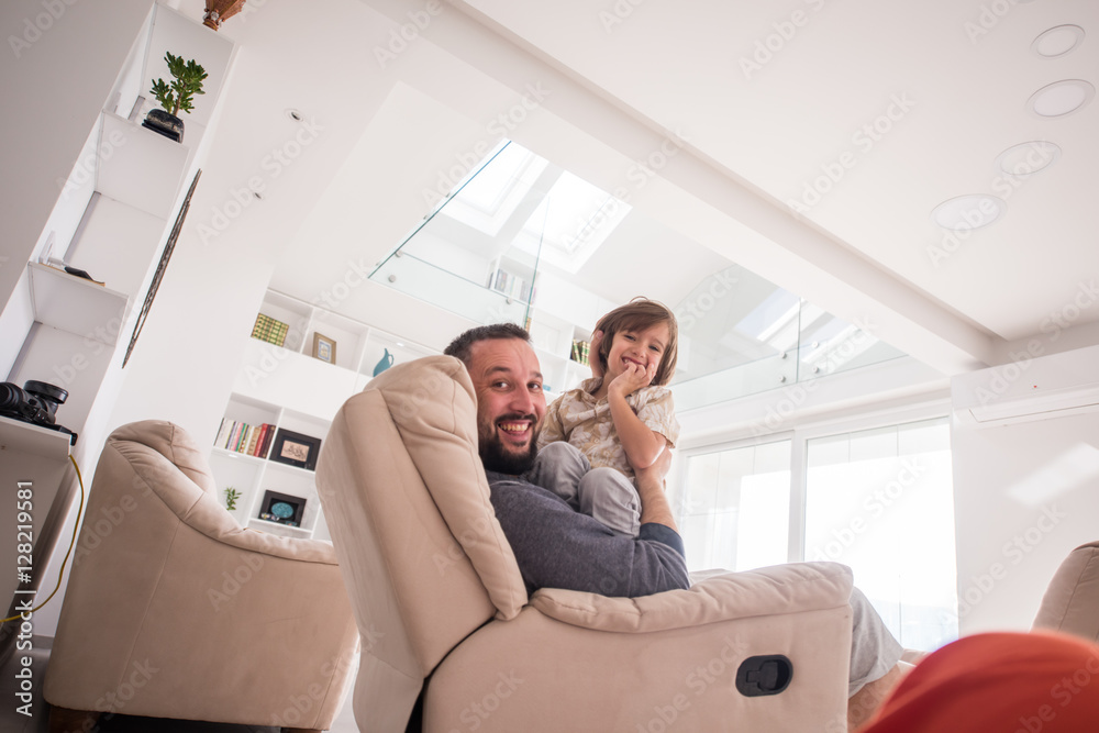 Cheerful young boy having fun with father on sofa