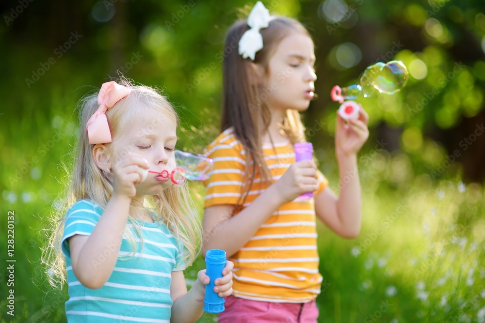 Two funny little sisters blowing soap bubbles outdoors