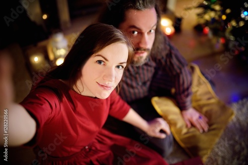 Young happy couple taking a photo of themselves by a fireplace on Christmas