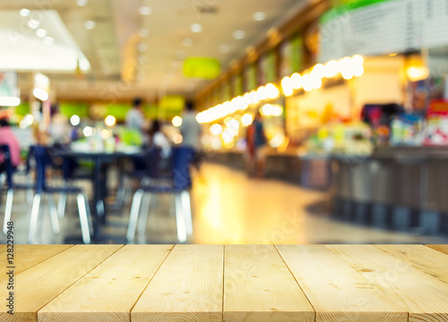 Food court or foodcourt interior blurred background. Restaurant or canteen with table, people at indoor plaza, mall, store or shopping center. Include empty wooden counter or desk for product display. photo