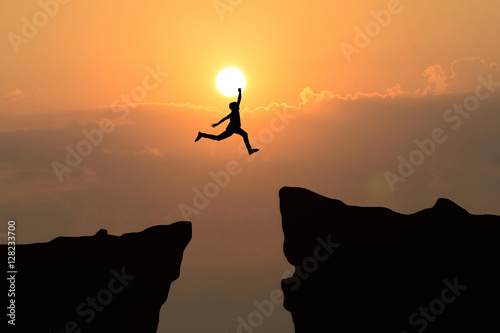Man jump through the gap between hill.man jumping over cliff on sunset background,Business concept idea