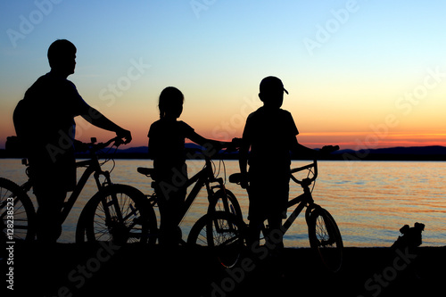 Image of sporty family on bicycles outdoors against sunset. Silh