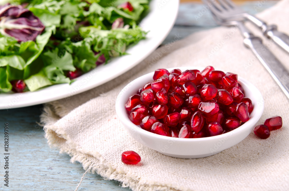 Green salad with spinach, frisee, arugula, radicchio and pomegranate seeds on blue wooden background Green salad with spinach, frisee, arugula, radicchio and pomegranate seeds on blue wooden background