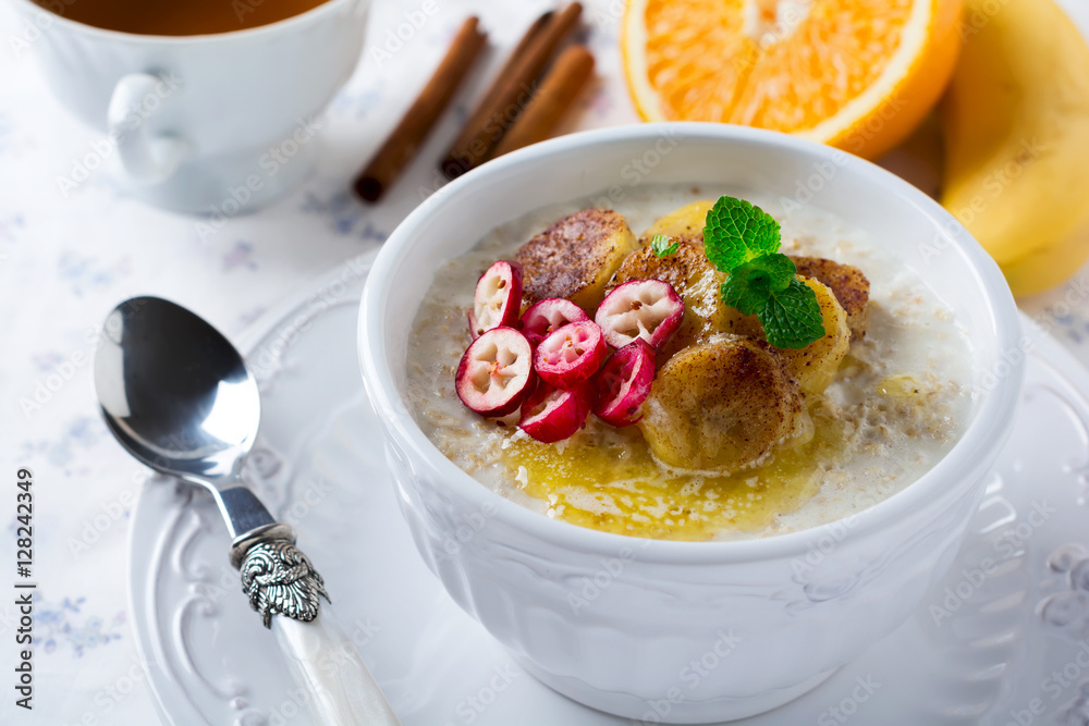 Oat porridge with baked bananas, cinnamon,orange and cranberries in a ceramic bowl for healthy breakfast on a light background. Selective focus. Oat porridge with baked bananas, cinnamon,orange and cranberries in a ceramic bowl for healthy breakfast on a light background. Selective focus.