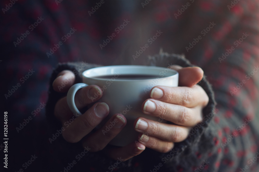 Woman in sweater hands holding a cup of warm coffee Woman in sweater hands holding a cup of warm coffee
