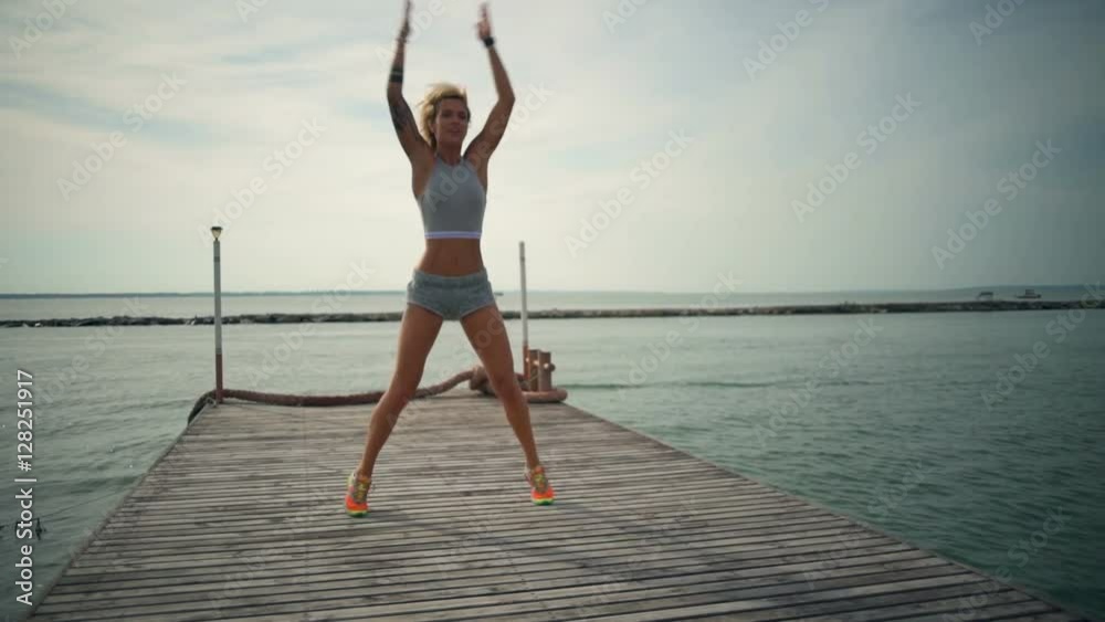 Young fit woman doing jumping jack exercise on the beach slow motion
