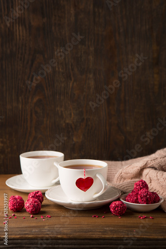 Two cups of hot tea and strawberry chocolate candies on rustic dark wooden background. Valentine's day celebration concept