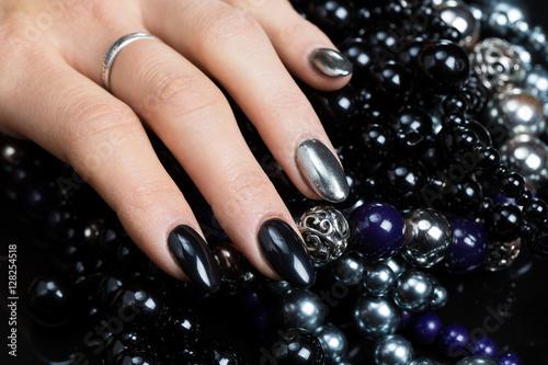 Beautiful female hands with nail polish black and silver color with black and silver beads on a black background