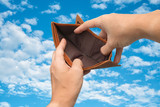 empty genuine leather wallet brown color in male hands, poor man looking for some money in the wallet from bankruptcy in the sky and clouds background.