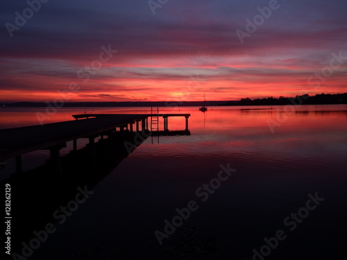 Steg am Ammersee bei Sonnenuntergang, rötlich gefärbtes Wasser 