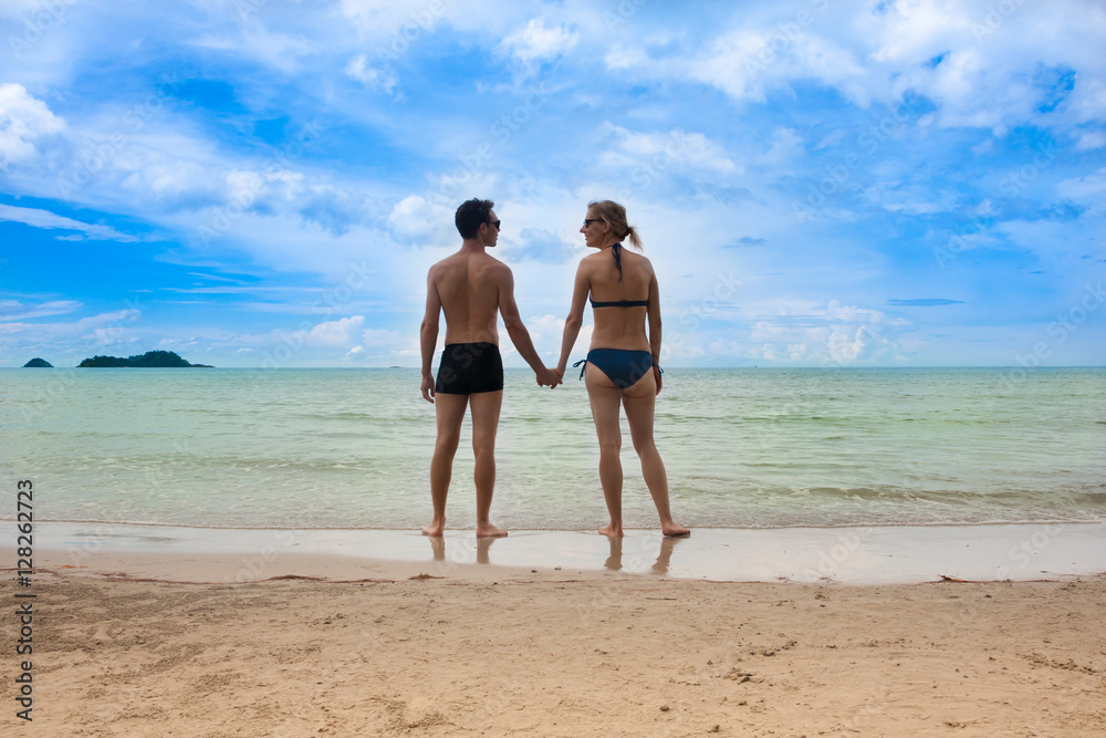Young couple on beautiful seabeach is standing and holding hands. Honeymoon vacation