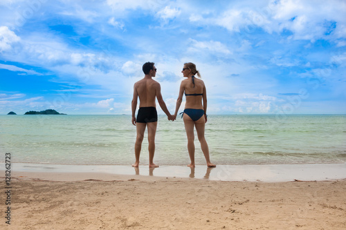 Young couple on beautiful seabeach is standing and holding hands. Honeymoon vacation
