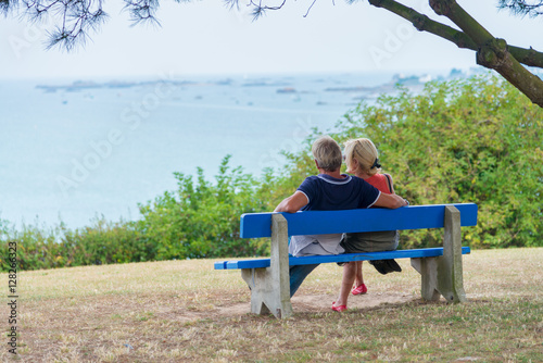ein Paar sitzt auf einer blauen Bank und schaut auf das Meer