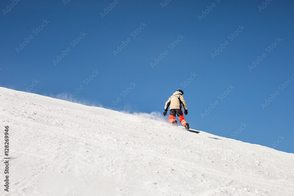 snowboarder going down on white snow slope against clear blue sky background