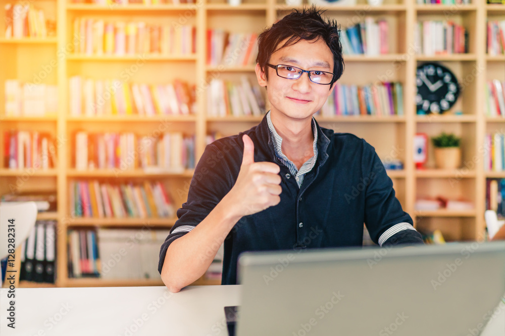 Φωτογραφία Young adult Asian man with laptop, thumbs up ok sign, home office or library sce