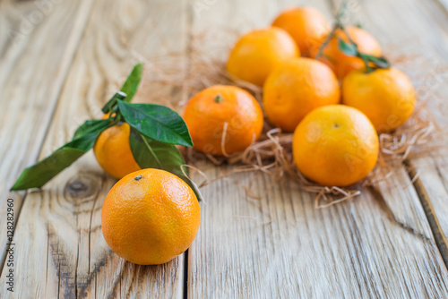 Some ripe tangerines with straw on wood background.