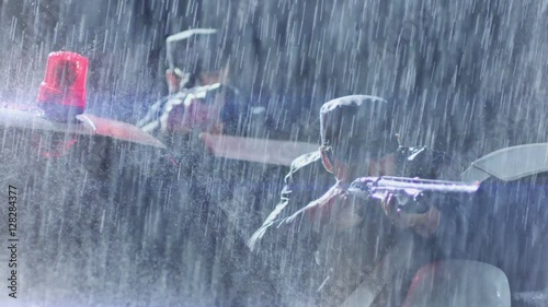 Armed policemen take aim to the offender. Another policeman speaks on rupper. Police surrounding on the rain.  photo