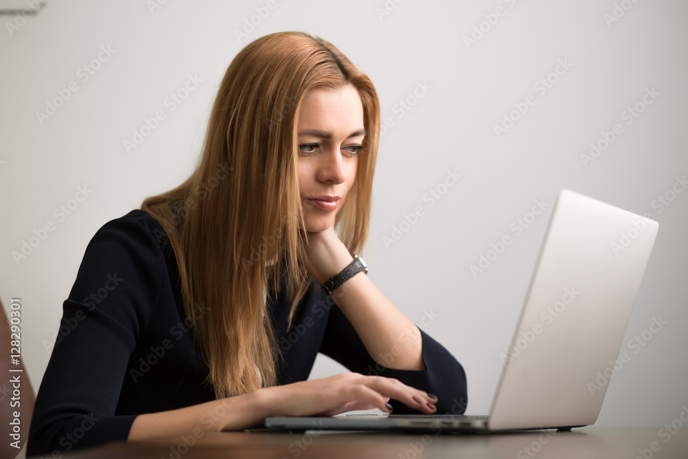 Businesswoman sitting at her workstation in office and working by notebook Businesswoman sitting at her workstation in office and working by notebook