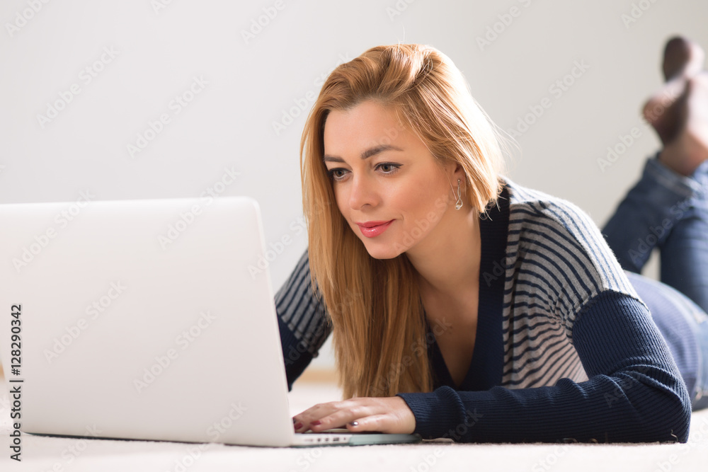 Beautiful adult woman lying on floor at home and using laptop Beautiful adult woman lying on floor at home and using laptop