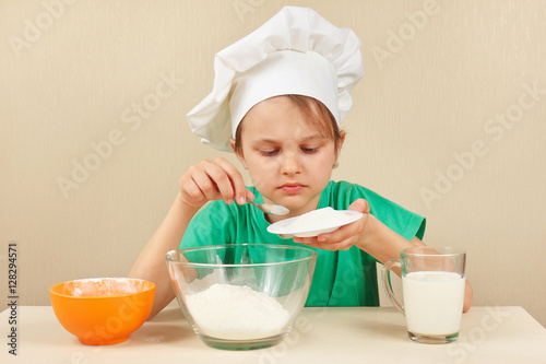 Young boy in chefs hat pours sugar for baking the cake