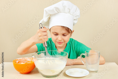 Little funny chef prepares the dough for baking the cake