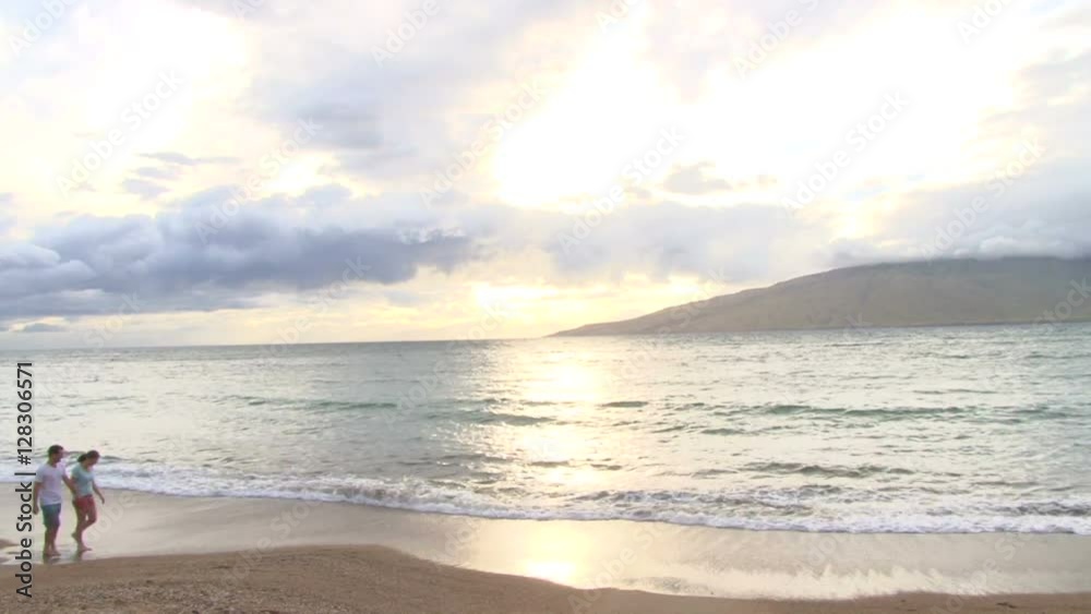 Model released couple walking hand in hand together on Hawaiian beach at sunset. Model released couple walking hand in hand together on Hawaiian beach at sunset.