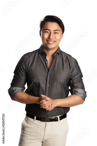 Relaxed good looking man standing against a white background wearing a grey shirt, smiling looking at camera.