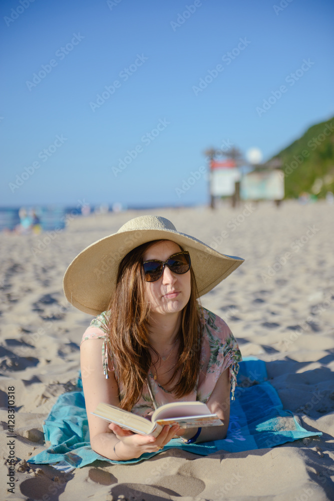Portrait of a young brunette relaxing on the beach, reading a book