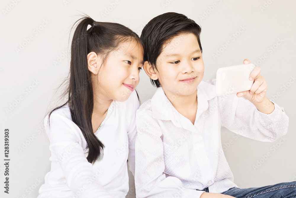 Lovely Asian couple school kids are taking selfie, 7 and 10 years old, over gray background Lovely Asian couple school kids are taking selfie, 7 and 10 years old, over gray background