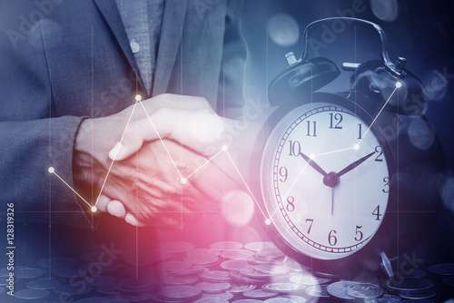 Double exposure of business man handshake with a row of stack money coins and analog clock with business graph information diagram concept for business finances and saving money.