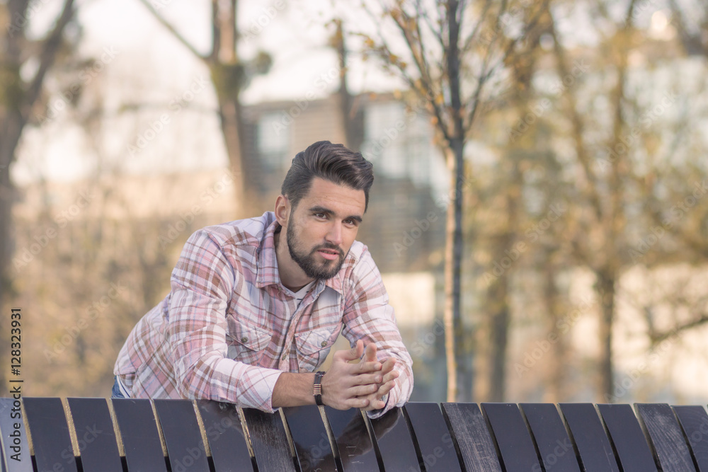 Fototapeta premium Young adult man leaning on bench, outdoors head, face.
