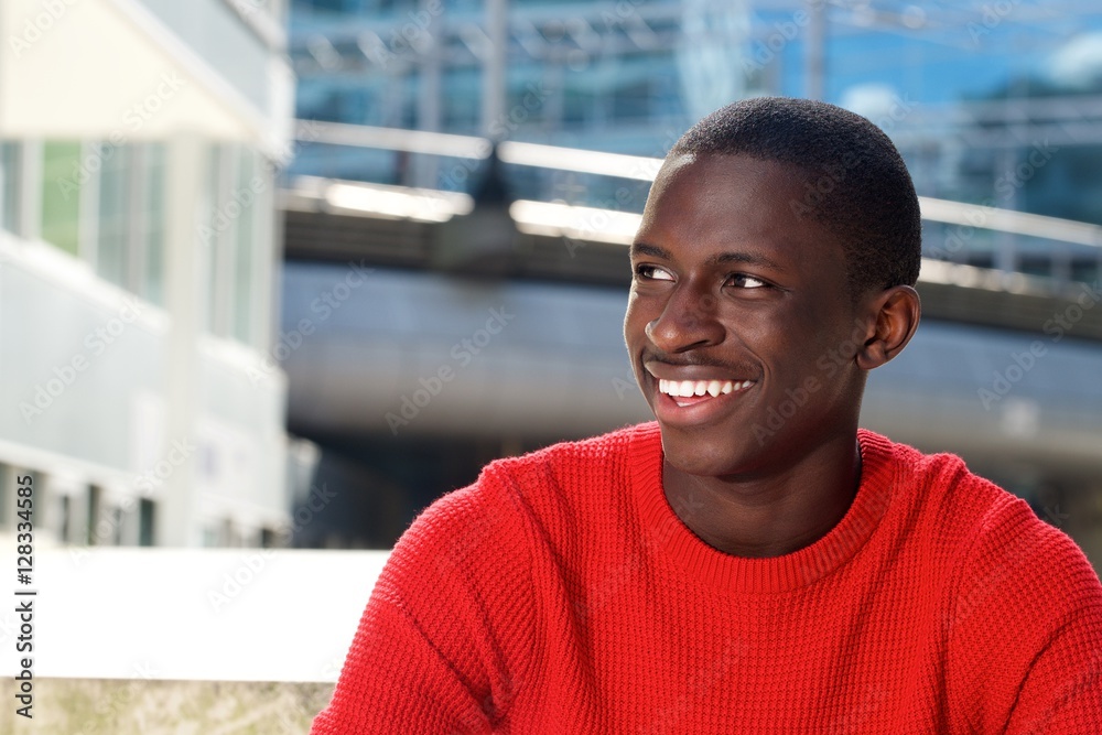 Happy young african guy sitting outdoors and looking away
