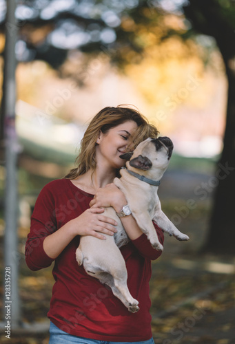 People and dogs outdoors. Portrait of beautiful and happy woman enjoying in autumn park walking with her adorable French bulldog.