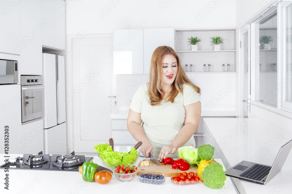 Fat woman making salad with laptop