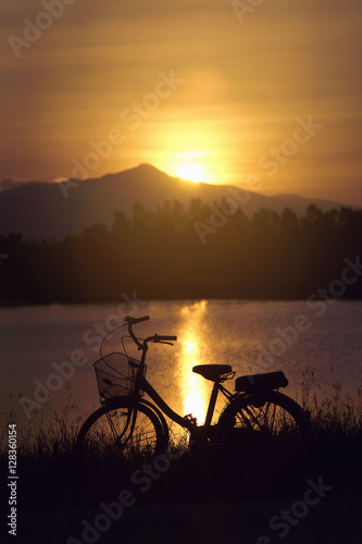 retro vintage bicycle near the lake at sunset moment. silhouette bicycle at the sunset with grass field.big mountain and sunset background.journey concept.lonely concept © ittoilmatar