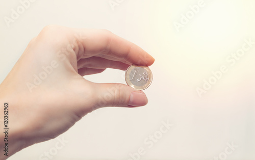 Woman's hand holding a coin one euro on white background. Business concept