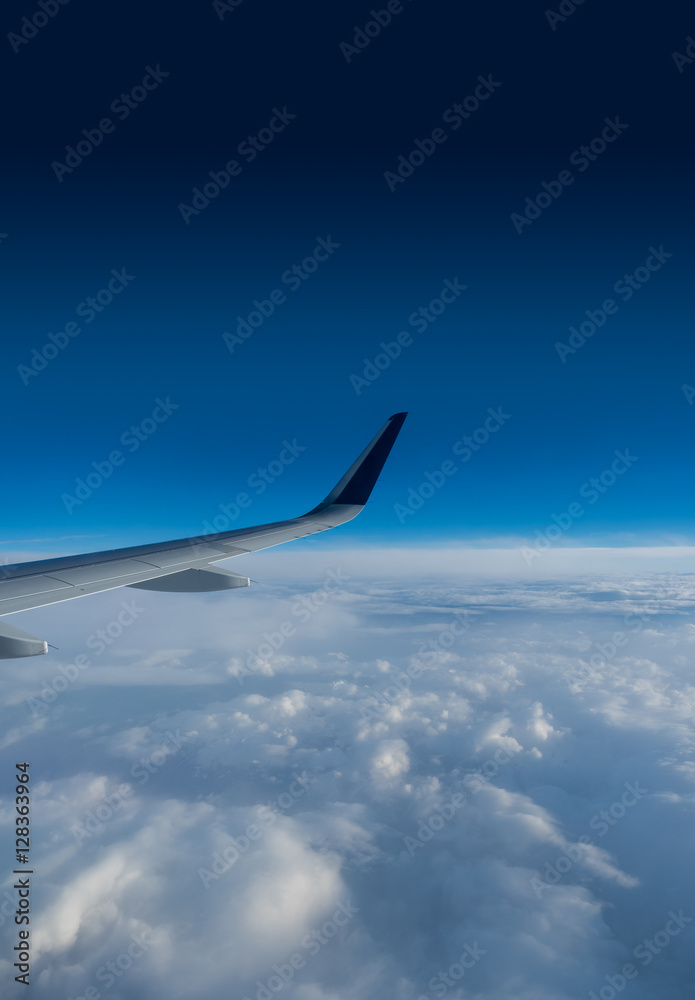 Fototapeta premium Wing of an airplane flying above the clouds on a clear sunny day