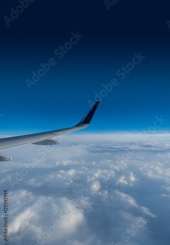 Wing of an airplane flying above the clouds on a clear sunny day