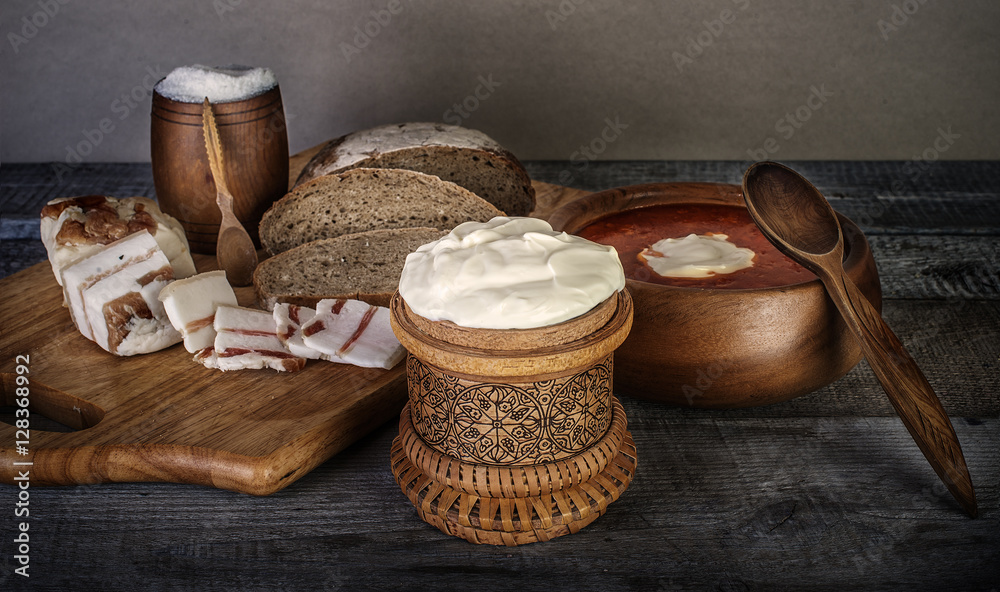 bowl of soup with sour cream, bread and bacon on wooden table