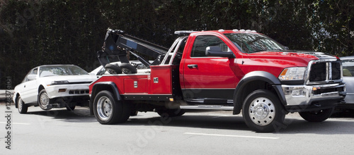 Surprise! Your car is G-O-N-E! Red tow truck hauling away white car. Horizontal. photo
